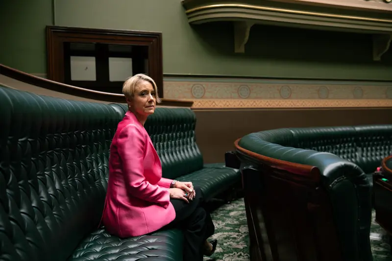 A white woman in a pink blazer sits on a curved leather bench.